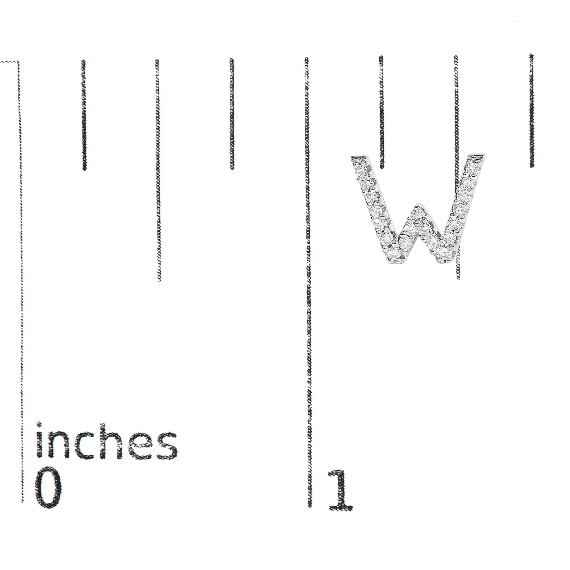 Close-up of a white metal earring shaped as the letter W, adorned with round white gemstones in micro-pave setting, shown on a ruler for scale from a top angled view.