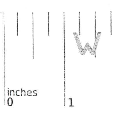 Close-up of a white metal earring shaped as the letter W, adorned with round white gemstones in micro-pave setting, shown on a ruler for scale from a top angled view.