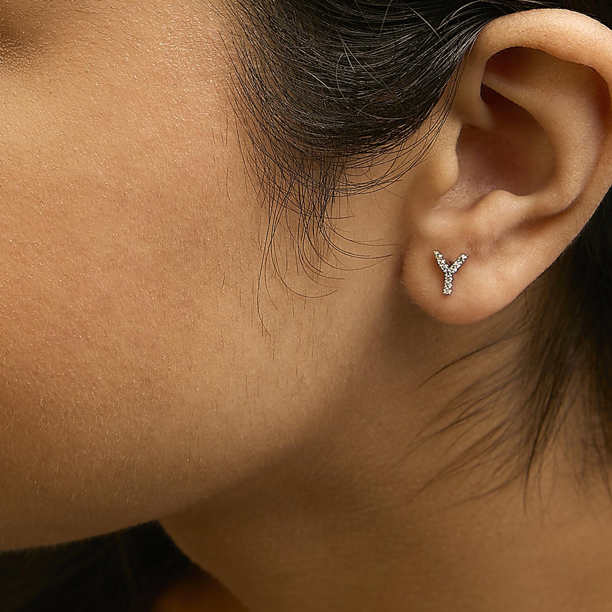 Close-up side view of a model wearing white metal earrings shaped like the letter Y, adorned with small round white gemstones in a micro-pave setting.