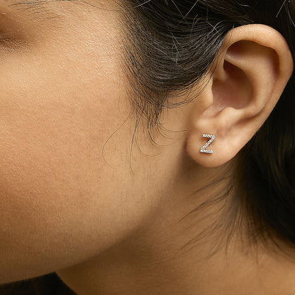 Close-up side view of a model wearing a white metal earring shaped like the letter 'Z' with micro-pave set round white gemstones.