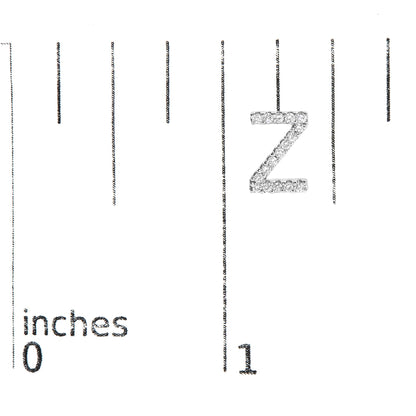 Close-up front view of a single white metal earring shaped like the letter Z, encrusted with round white gemstones in a micro-pave setting, shown on a scale with inch markings.