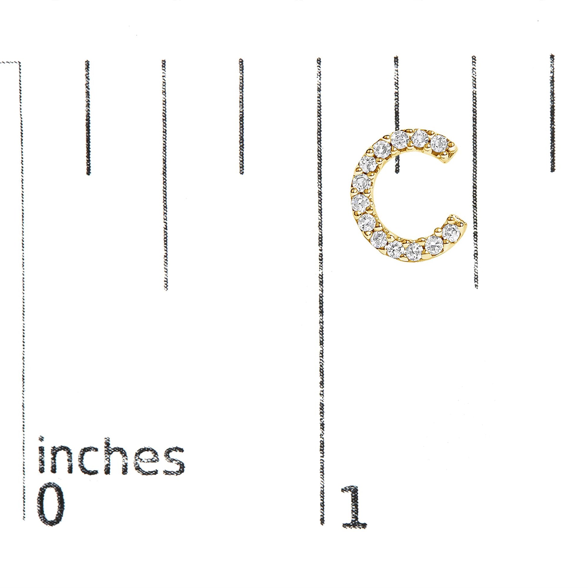 Close-up front view of a yellow metal C-shaped earring with round white gemstones in a micro-pave setting, shown on a scale.
