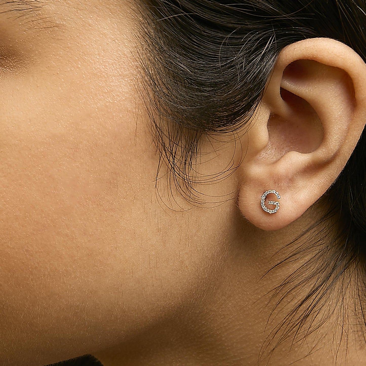 Close-up side view of a model wearing a yellow metal earring in a partial circular shape encrusted with small white gemstones in a micro-pave setting.