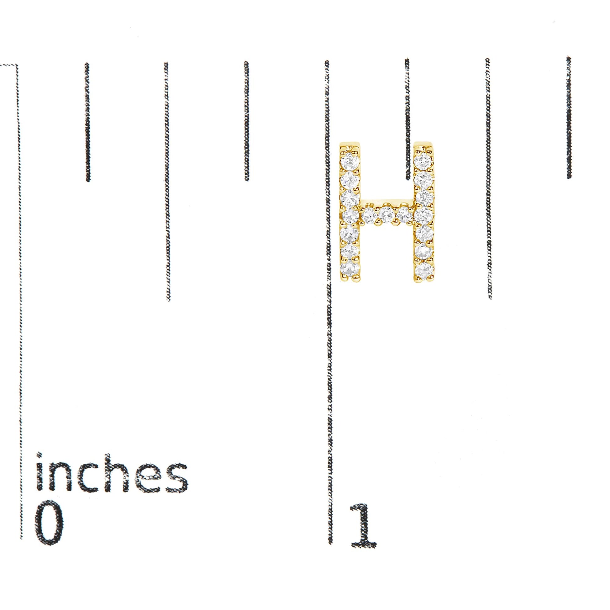 Close-up image of a yellow metal earring in the shape of the letter 'H' with round white gemstones in micro-pave setting, shown on a scale with inches markings, shot from the front.