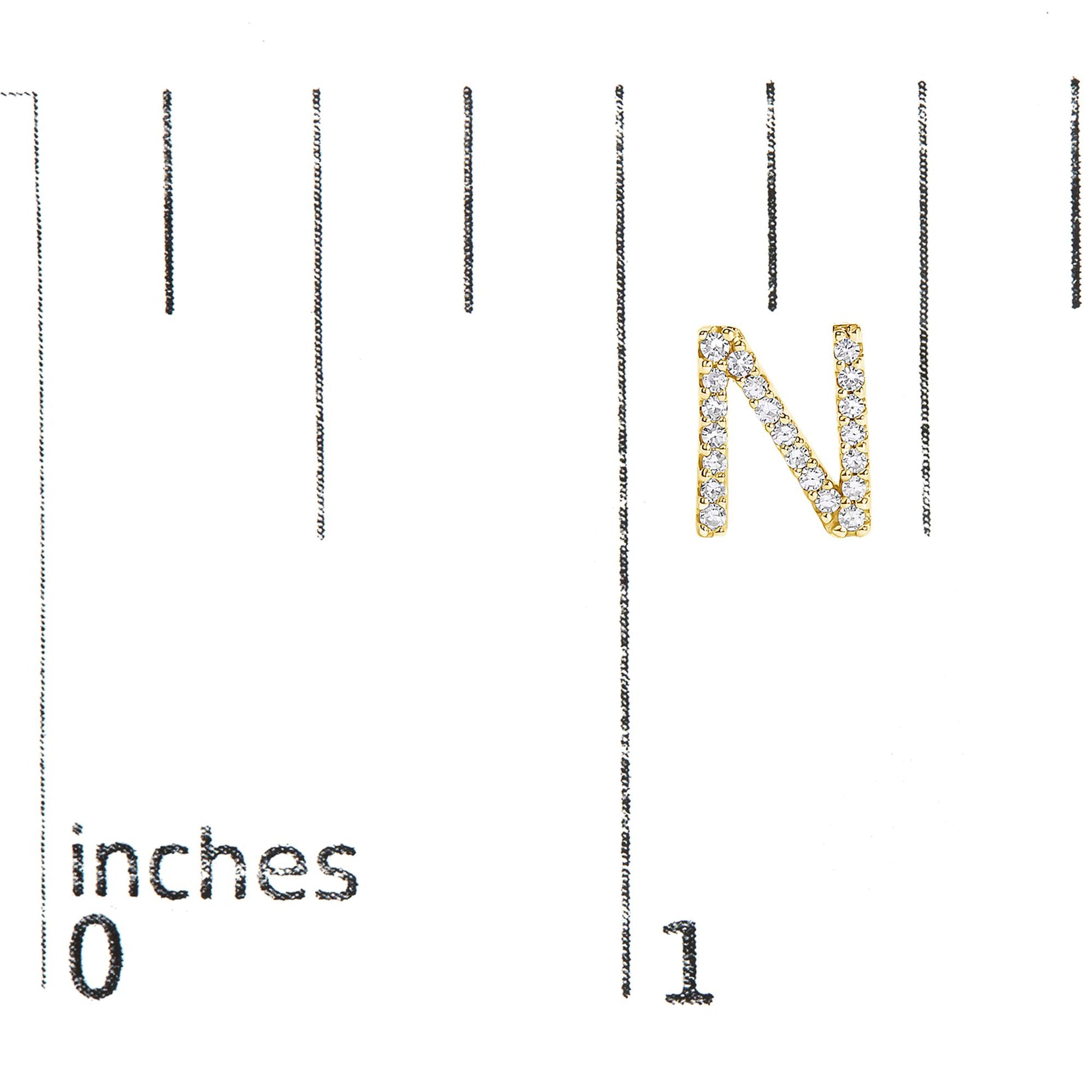 Close-up of a yellow metal earring shaped like the letter N, adorned with small white gemstones, shown on a scale with inch markings, photographed from the front.