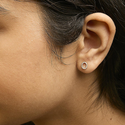 Close-up side view of a model wearing a small oval-shaped yellow metal earring with round white gemstones set in a micro-pave style.