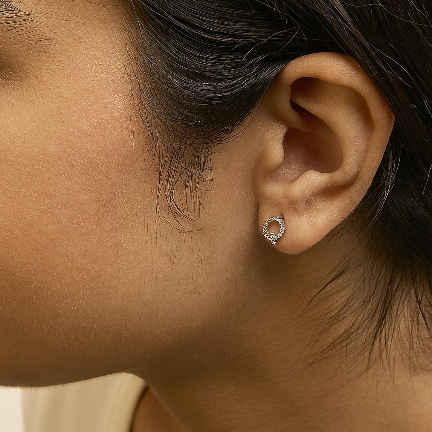 Close-up side view of a model wearing a pair of small yellow metal circular stud earrings with white round gemstones in a micro-pave setting.