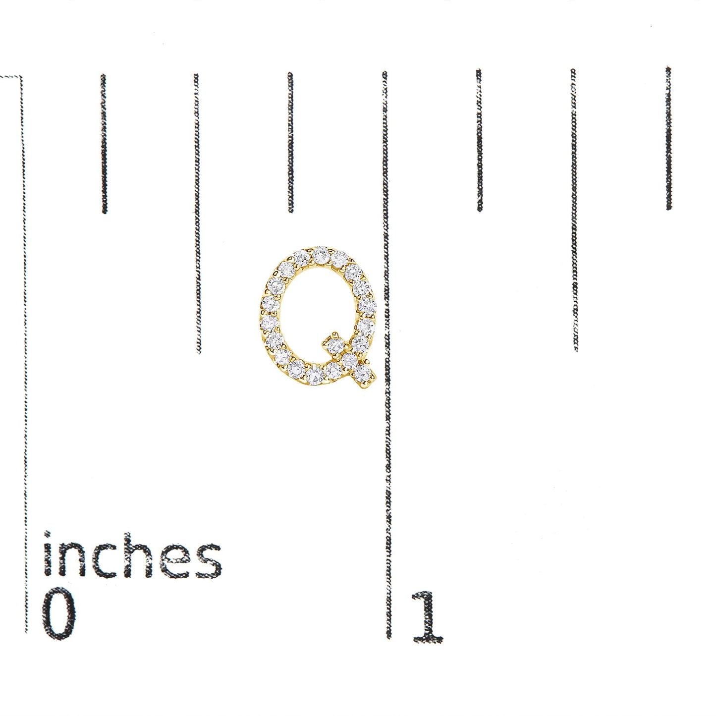Close-up of a yellow metal earring shaped like the letter Q adorned with round white gemstones, shown on a scale with inch markings, top-down angle.