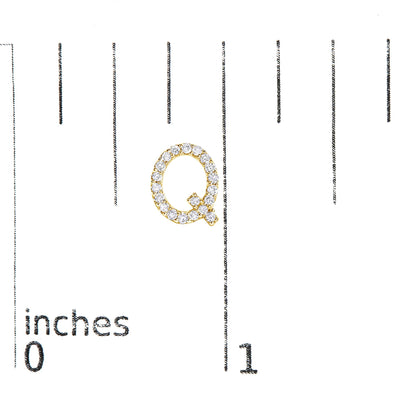Close-up of a yellow metal earring shaped like the letter Q adorned with round white gemstones, shown on a scale with inch markings, top-down angle.
