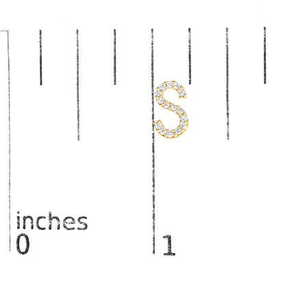 Close-up image of a yellow metal earring shaped like the letter 'S', adorned with small white round gemstones set in a micro-pave style, shown on a scale.