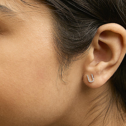 Close-up side view of a model wearing yellow metal earrings shaped like an open U, decorated with small white gemstones in a micro-pave setting.