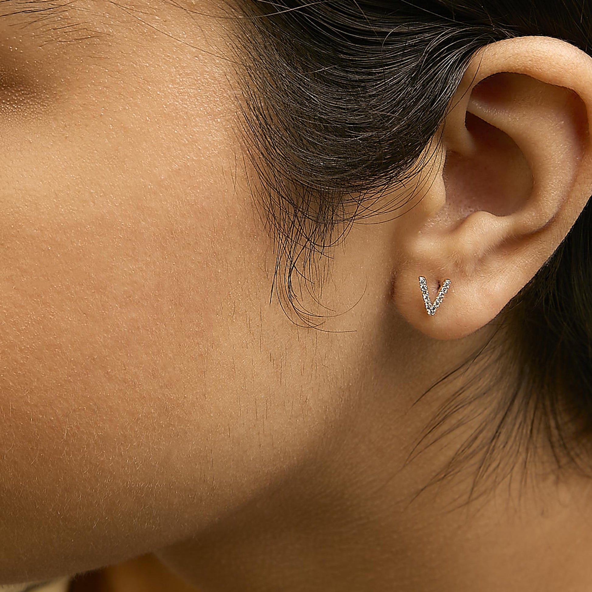 Close-up side view of a model wearing yellow metal V-shaped earrings with round white gemstones in a micro-pave setting.