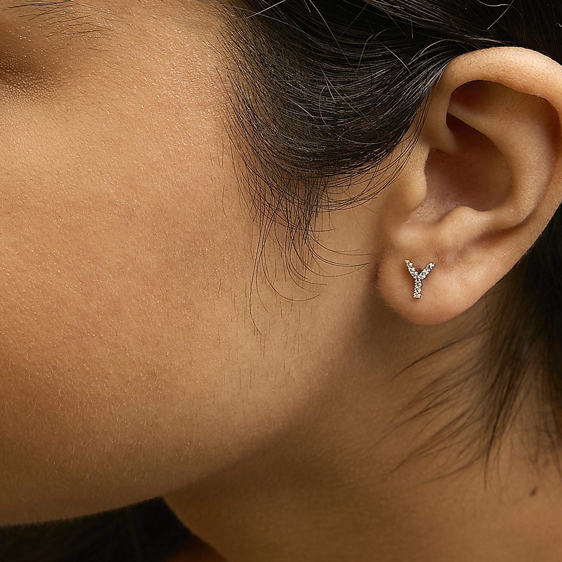 Close-up side view of a model wearing yellow metal earrings shaped like the letter Y, adorned with small white gemstones in a micro-pave setting.