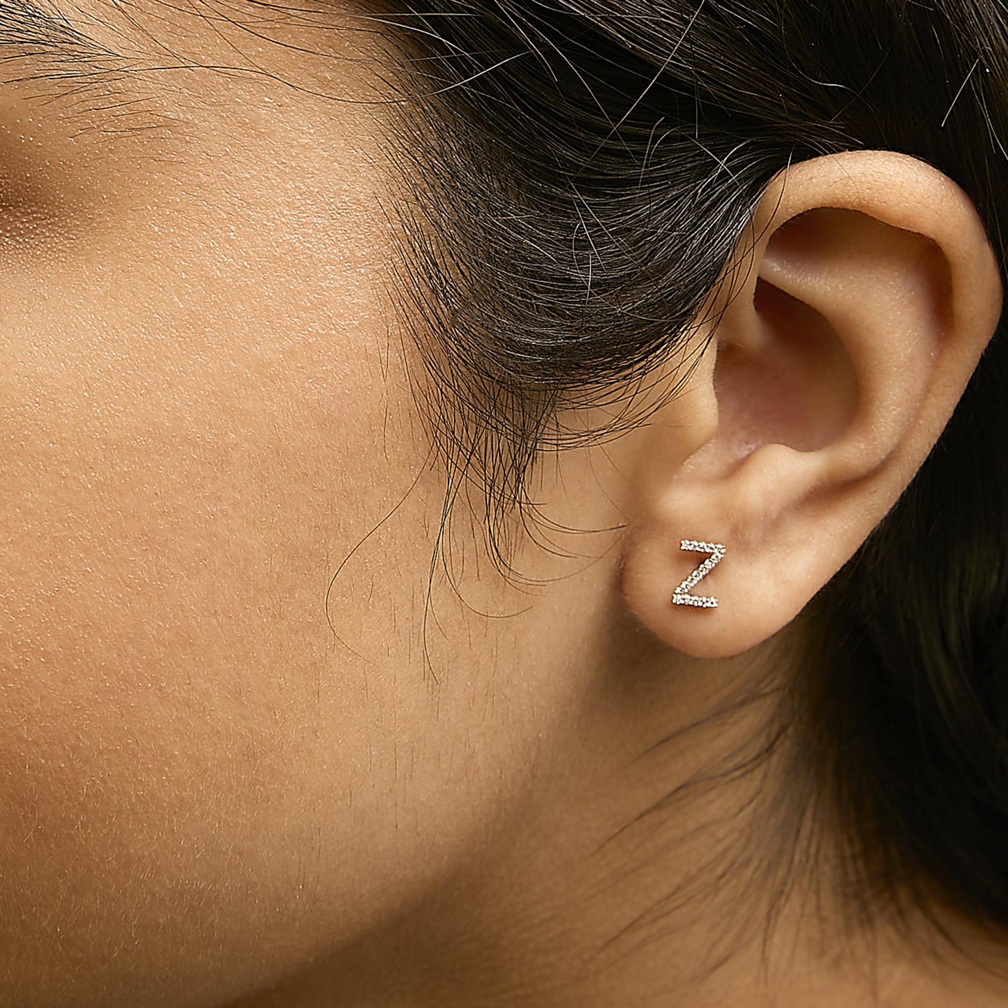 Close-up side view of a model wearing a yellow metal earring shaped like the letter Z, encrusted with small white gemstones in a micro-pave setting.