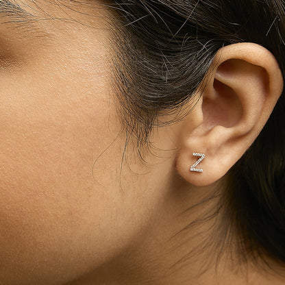 Close-up side view of a model wearing a yellow metal earring shaped like the letter Z, encrusted with small white gemstones in a micro-pave setting.