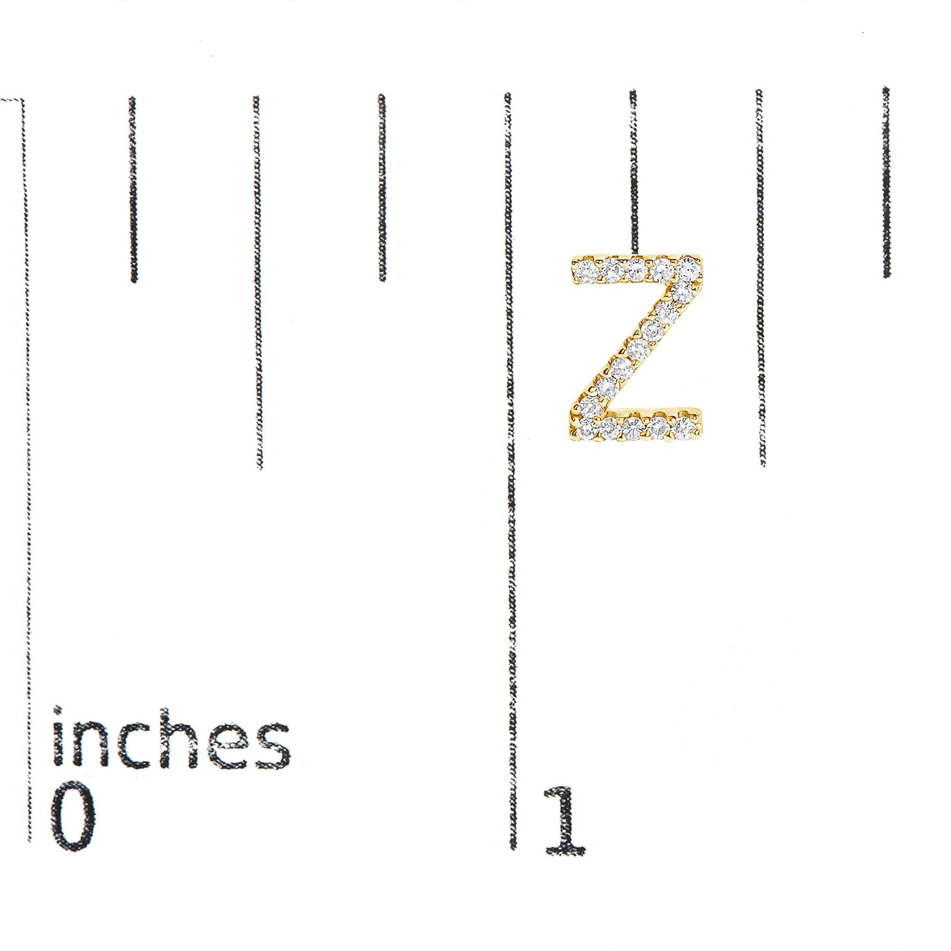 Close-up front view of a yellow metal letter Z-shaped earring with round white gemstones in micro-pave setting, shown on a scale marked in inches.