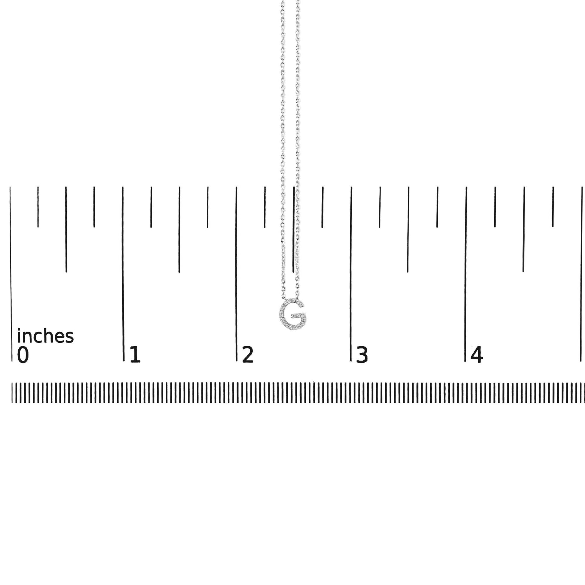 Close-up front view of a white necklace chain with a pendant shaped like the letter G, encrusted with small white gemstones, shown on a ruler scale.