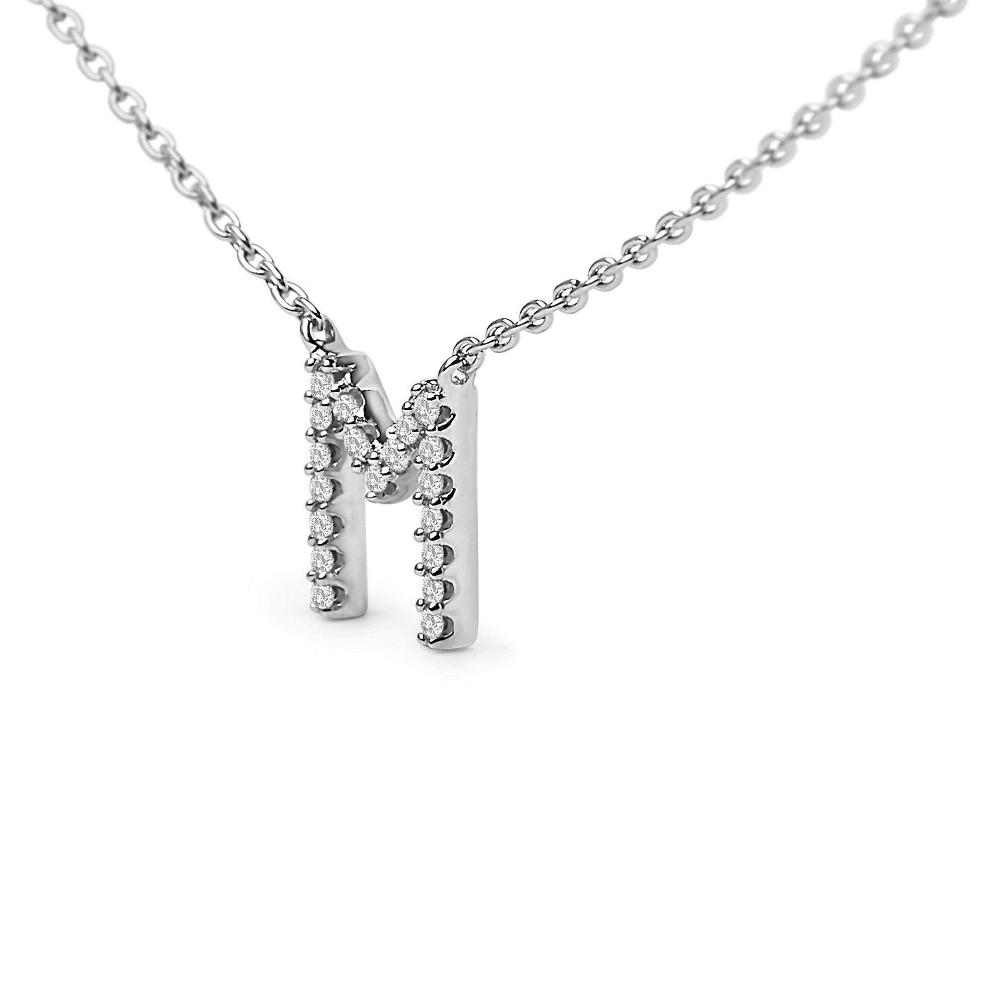 Close-up front view of a white metal necklace pendant in the shape of the letter M, adorned with round white gemstones in a micro-pave setting, shown on a white background.