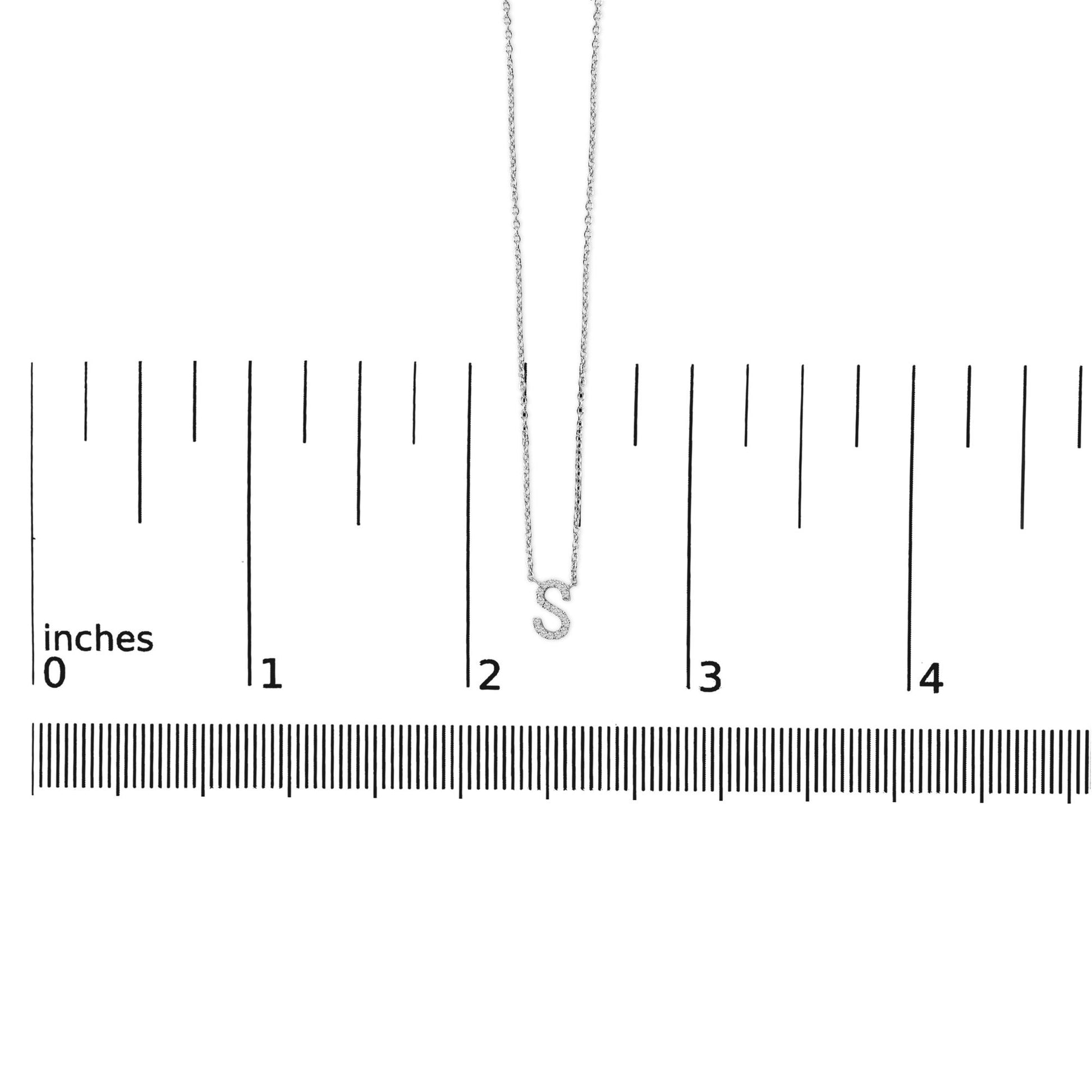 Close-up front view of a white metal necklace with an 'S' shaped pendant featuring micro-pave set round white gemstones, shown on a measurement scale.