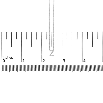 White metal necklace with a Z-shaped pendant set with small white gemstones, shown hanging vertically on a ruler scale, front view.