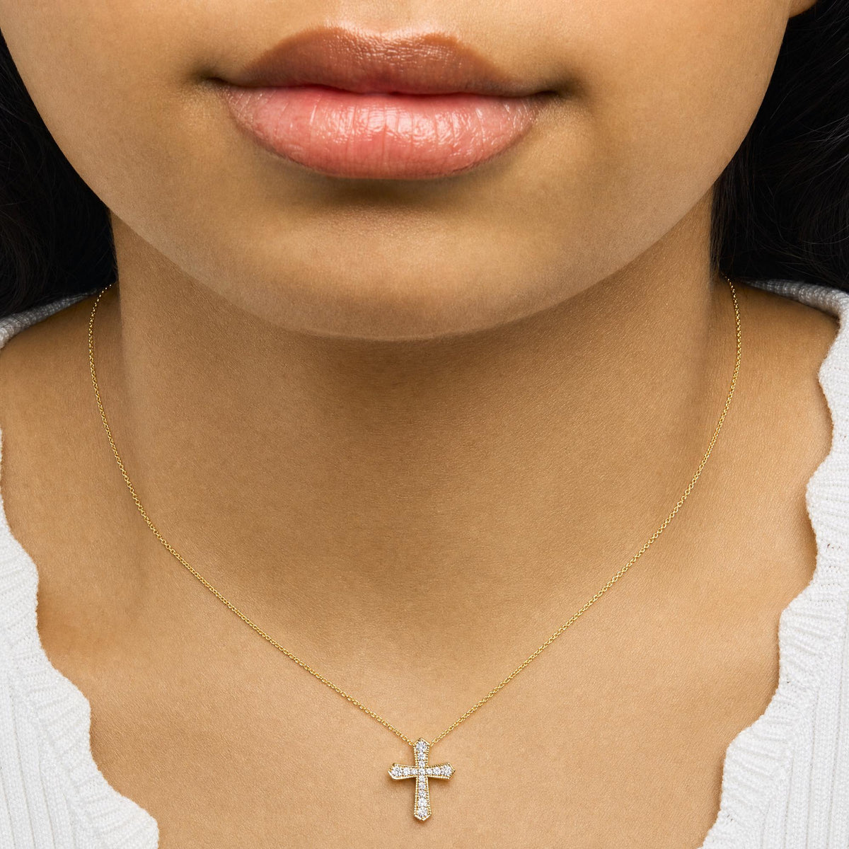 Close-up front view of a model wearing a yellow metal necklace with a cross-shaped pendant featuring white round gemstones in a pave setting.