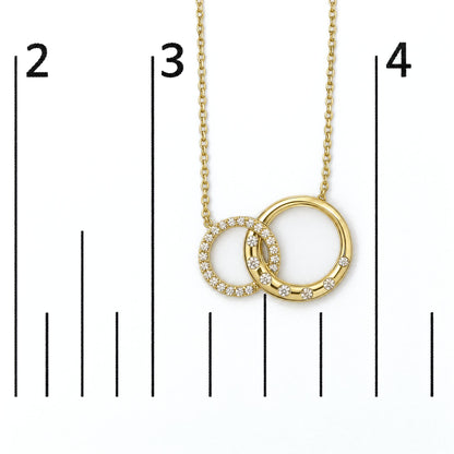 Close-up front angle image of a yellow necklace with two interlocking circles, one circle fully adorned with white gemstones and the other partially adorned, shown on a scale.