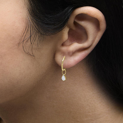 Close-up side view of a model wearing a yellow metal earring with a pear-shaped white gemstone in bezel setting, hanging from a small hoop.
