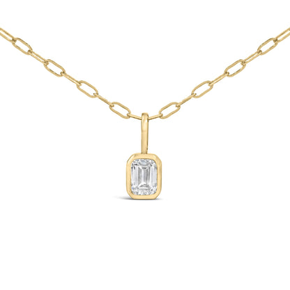 Close-up front angle of a yellow metal necklace with an emerald-shaped white gemstone in a bezel setting pendant.