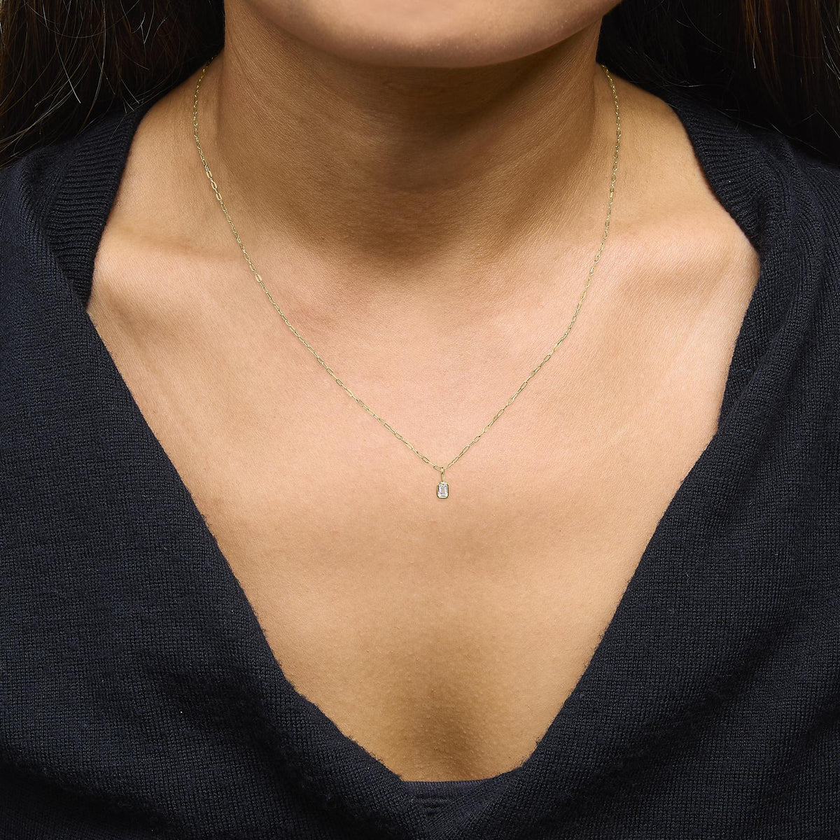 Close-up front view of a model wearing a yellow metal necklace with a rectangular white gemstone in a bezel setting pendant.