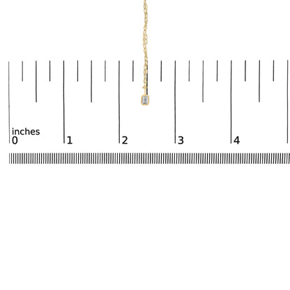 Close-up front view of a yellow metal necklace displayed on a scale, featuring a small emerald-shaped white gemstone in a bezel setting at the pendant's end.