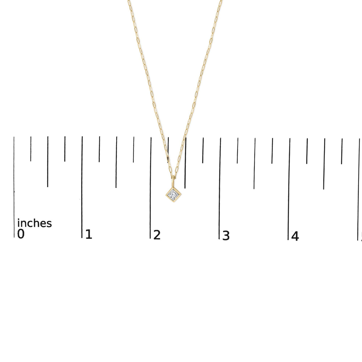 Close-up front view of a yellow metal necklace shown on a scale with a princess shape white gemstone in a bezel setting pendant.