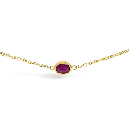 Close-up front angle of a yellow necklace with a single oval red gemstone in a bezel setting on a chain.