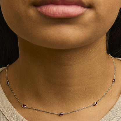 Close-up front view of a model wearing a delicate yellow necklace featuring multiple oval red gemstones in bezel settings evenly spaced along the chain.