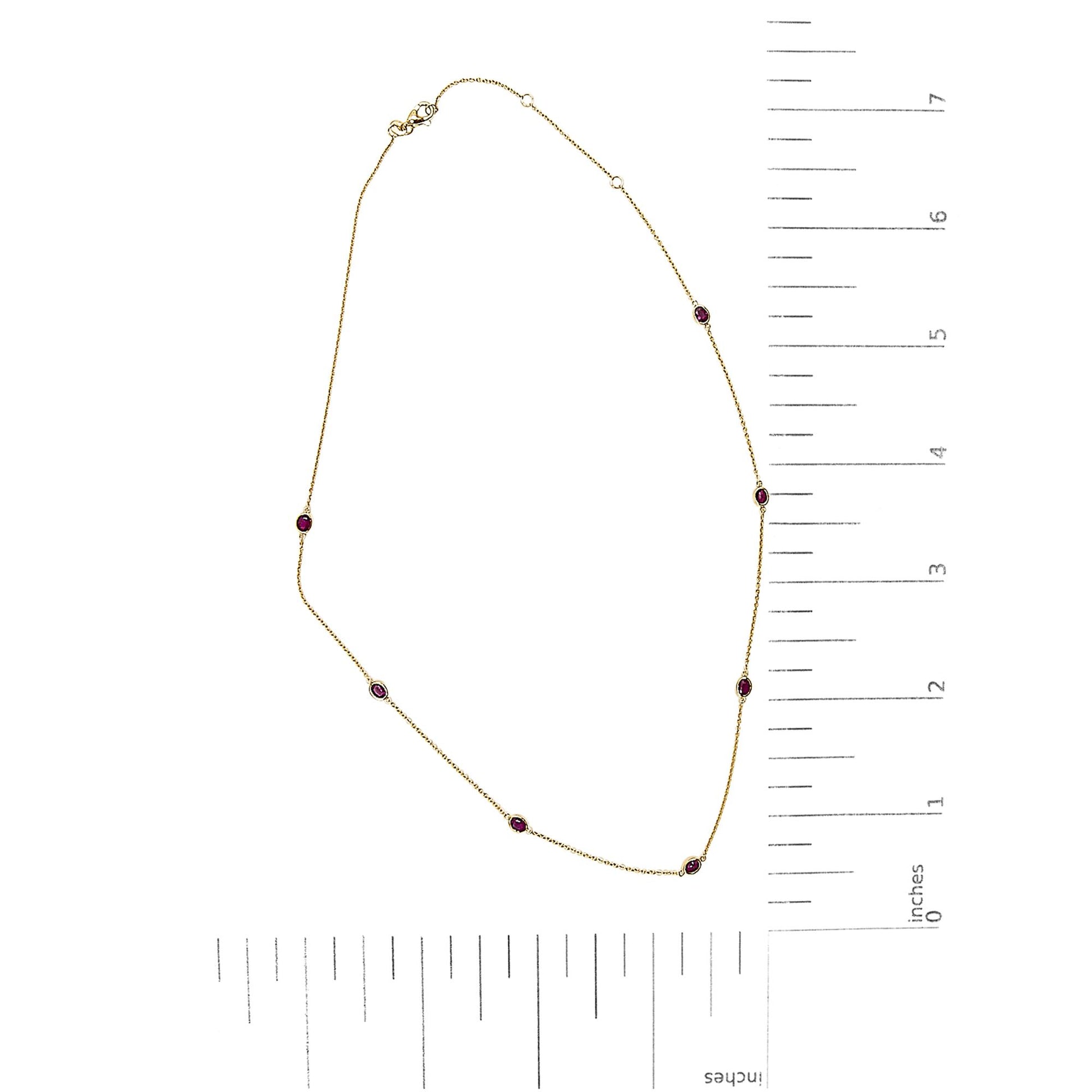 Yellow necklace with seven oval red gemstones in bezel settings shown flat on a white surface with rulers for scale, top-down angle.