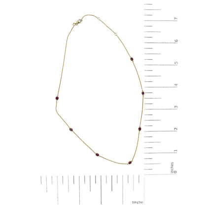 Yellow necklace with seven oval red gemstones in bezel settings shown flat on a white surface with rulers for scale, top-down angle.