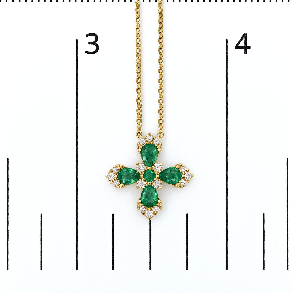 Yellow metal necklace with a cross-shaped pendant featuring green pear and round gemstones surrounded by white round gemstones. Necklace shown on a scale, front-facing shot.