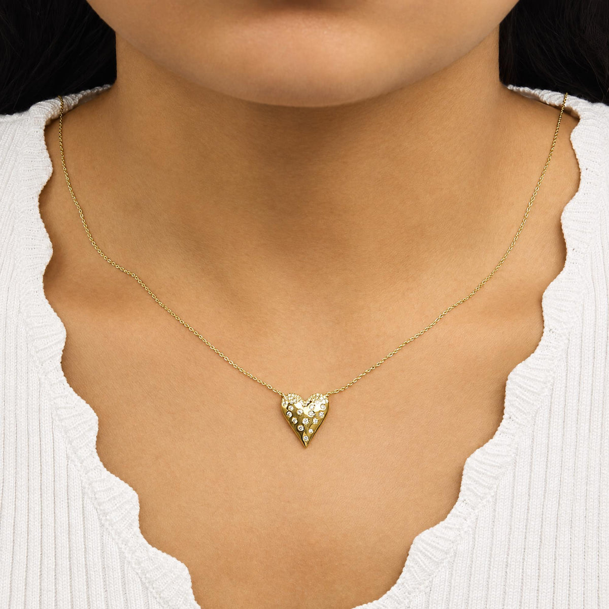 Close-up front view of a model wearing a yellow metal necklace with a heart-shaped pendant featuring scattered white gemstones in a pave setting.