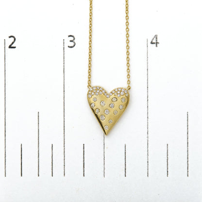 Close-up front view of a yellow metal heart-shaped necklace pendant adorned with multiple white round gemstones in pave setting, shown on a measurement scale.