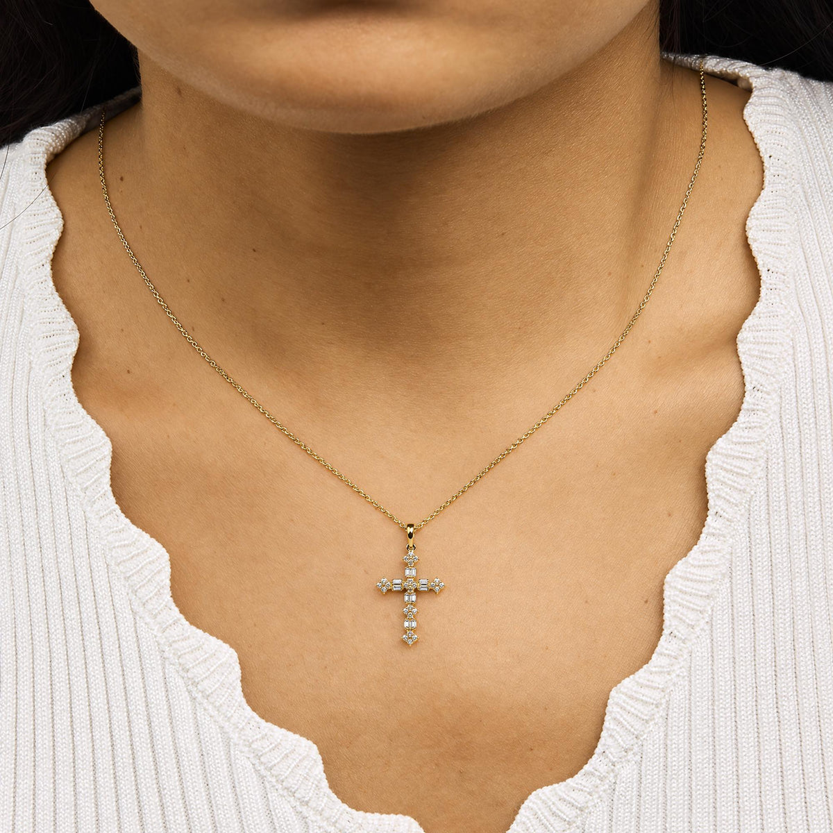 Yellow necklace with a cross pendant featuring white round and baguette gemstones in prong settings, shown worn on a model from a front angle.