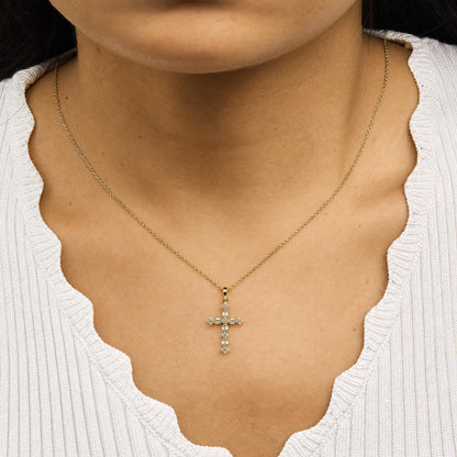 Yellow necklace with a cross pendant featuring white round and baguette gemstones in prong settings, shown worn on a model from a front angle.