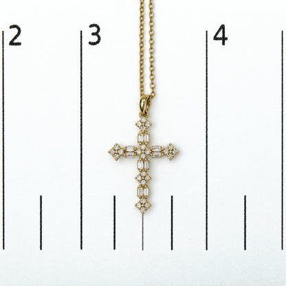 Close-up front view of a yellow metal cross-shaped necklace pendant with round and baguette white gemstones in prong settings, shown on a scale.