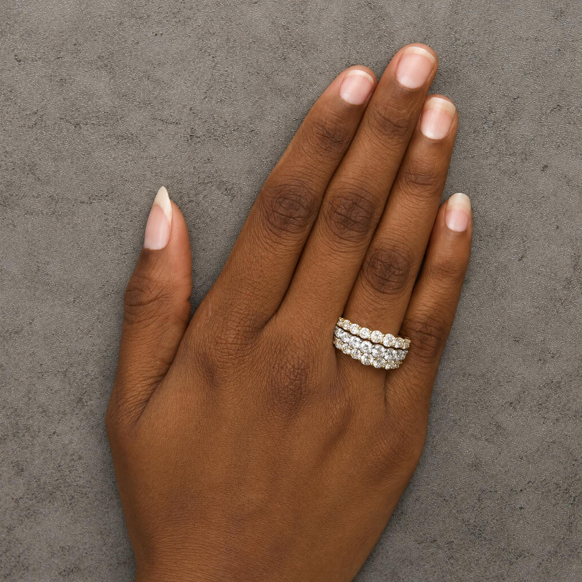 Close-up of a model's hand wearing two stacked rings featuring round white gemstones in a prong setting on yellow and white metal, shot from above.