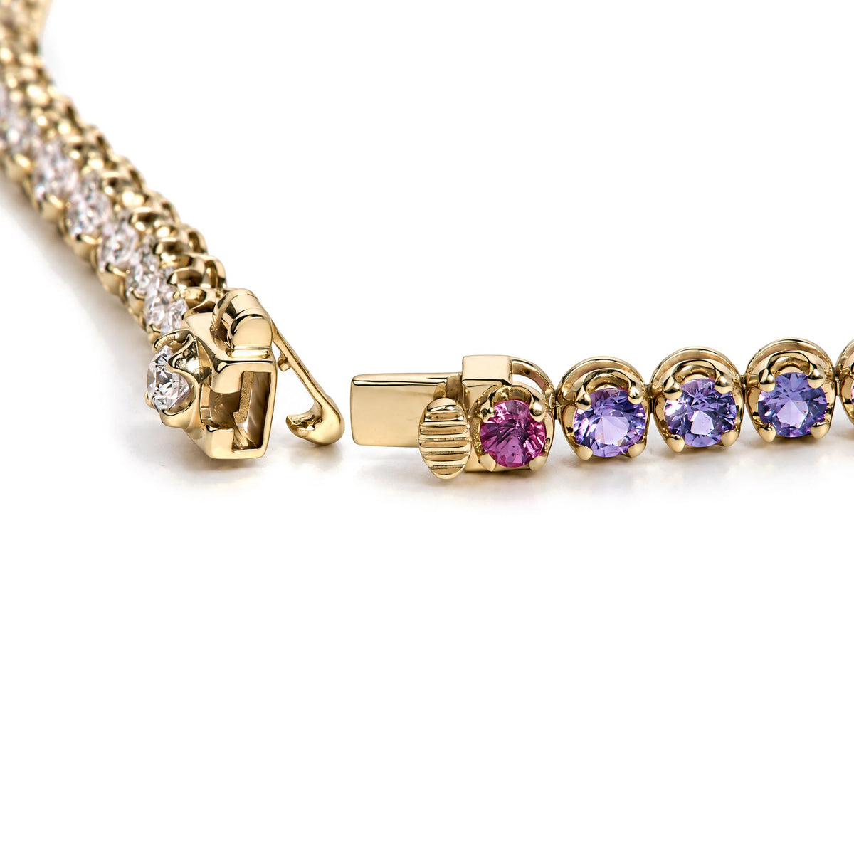 Close-up image of a yellow metal bracelet laid flat, featuring round white gemstones in prong settings along one side and round pink, purple, green, and yellow gemstones in prong settings along the other. The image is taken from an angled top view, focusing on the clasp and detailed settings of the stones.