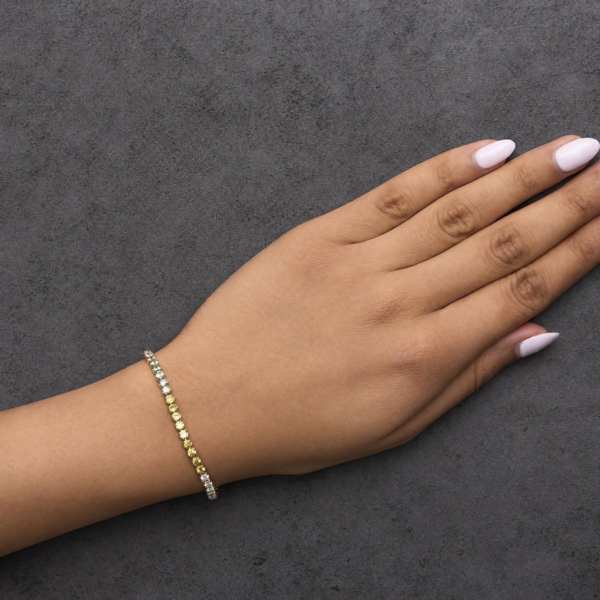 Bracelet with alternating round white gemstones and yellow gemstones in prong setting on a yellow metal band, shown worn on a model's wrist, angled top-down.