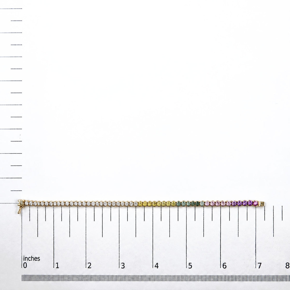 Yellow metal bracelet with round white gemstones followed by yellow, green, pink, and purple round gemstones, all prong-set, shown flat on a white scale with inch and centimeter markings, front view.