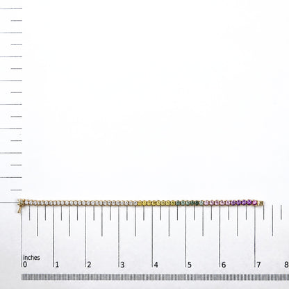 Yellow metal bracelet with round white gemstones followed by yellow, green, pink, and purple round gemstones, all prong-set, shown flat on a white scale with inch and centimeter markings, front view.