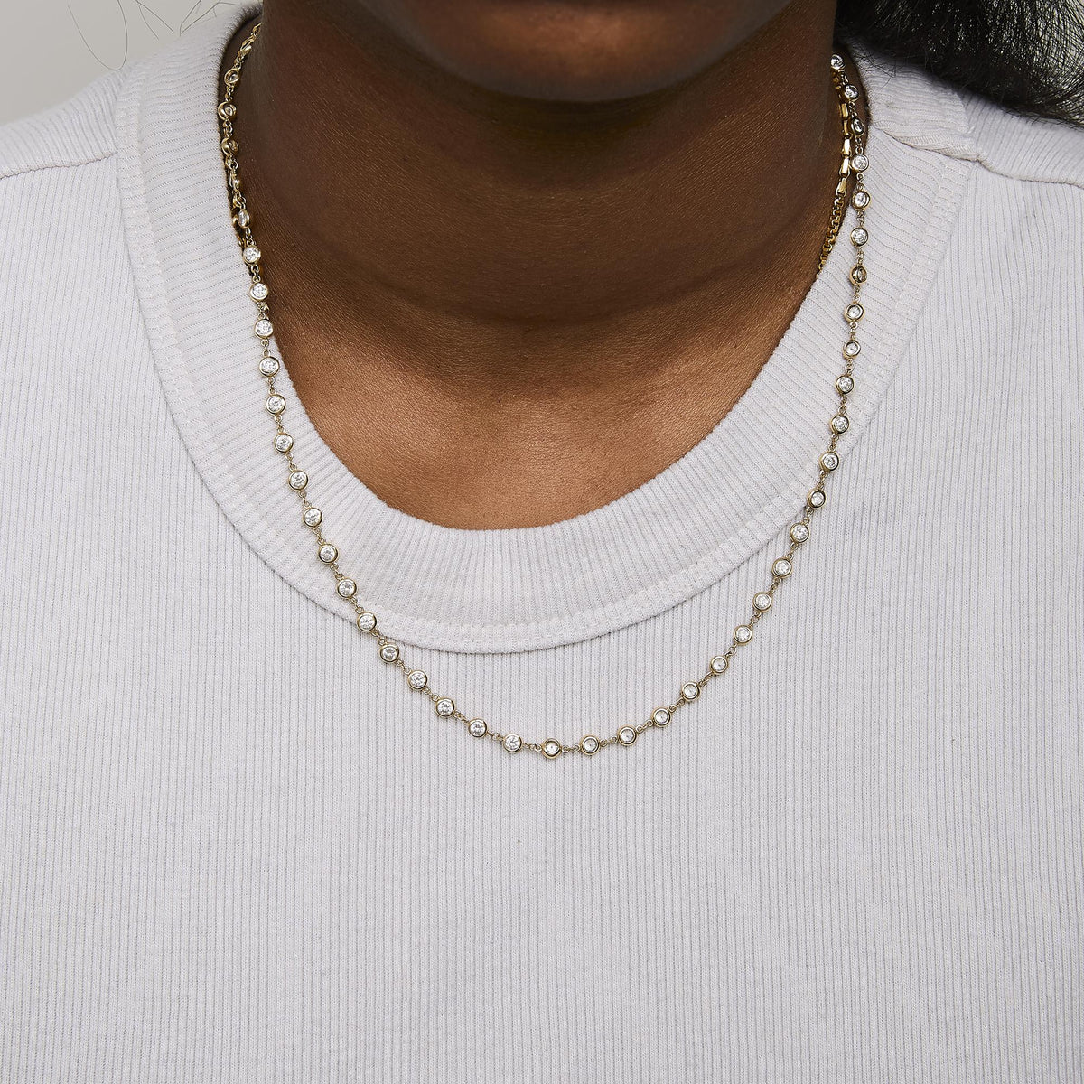 Close-up front view of a model wearing a yellow necklace featuring round bezel-set white gemstones evenly spaced along the chain.