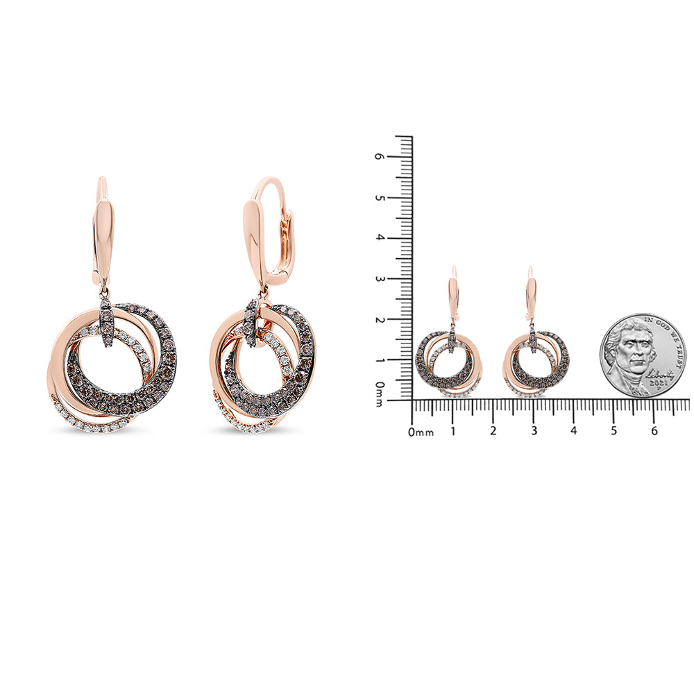 Rose metal earrings with intertwined circular loops, adorned with white and brown round gemstones in pave and prong settings, shown in a front-facing view and alongside a ruler and coin for size reference.