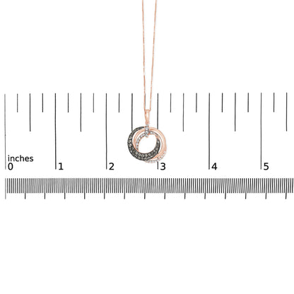 Rose metal necklace with two intertwined circular pendants, one set with white gemstones and the other with brown gemstones, shown front-facing on a ruler for size reference.
