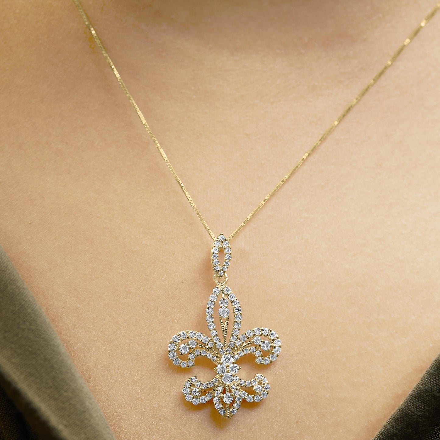 Close-up front view of a yellow metal necklace with a large ornamental pendant featuring numerous white round gemstones in prong settings, worn on a model.